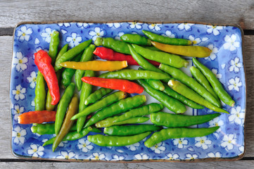 Many red and green Thai Chillis in plate on wooden table.