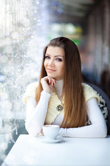 pretty young woman sitting in the cafe with a cup of coffee