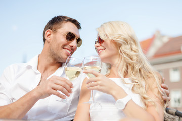 smiling couple in sunglasses drinking wine in cafe