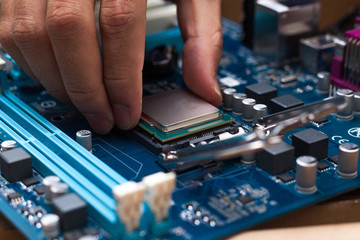 Obraz premium Assembling high performance personal computer, inserting CPU, processor into the motherboard socket, opened PC case in background, shallow depth of field, focus on hand