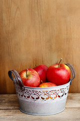 Silver bucket of red apples on wooden table. Copy space