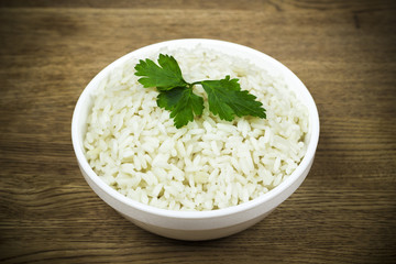 Plate of boiled rice with fresh herbs on a wooden texture