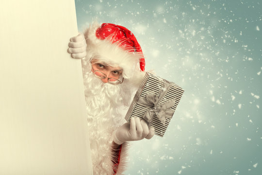 Santa Claus  from behind white blank banner holding a gift