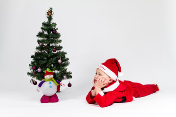 Dreaming baby boy dressed as Santa Claus lying next to Christmas