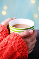 Hands holding mug of hot drink, close-up, on bright background