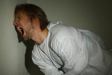 Mentally ill man in strait-jacket in room corner