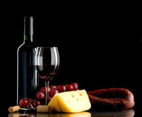 Wine, grapes, cheese and sausage on black background