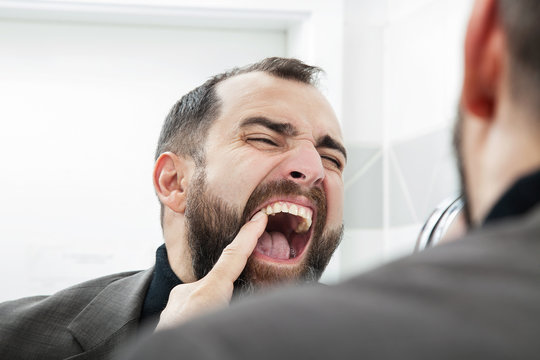 Man touching his tooth- looking in the mirror.