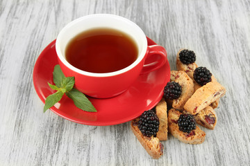 Cup of tea with cookies and blackberry on table close-up