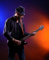 Obraz premium Young musician playing guitar on dark color background