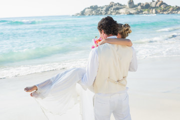 Handsome groom carrying his beautiful wife out to the water
