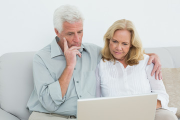 Relaxed senior couple using laptop on sofa