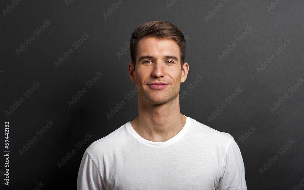 Wall mural handsome man posing in white tshirt on dark background in studio