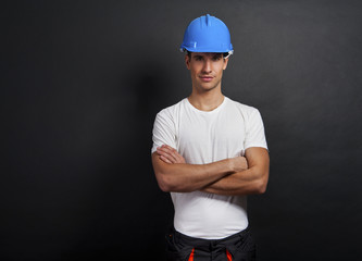 Young construction worker in hard hat on dark background