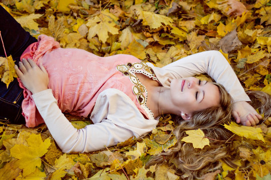 Beautiful happy pregnant woman lying with autumn leaves