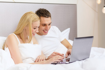smiling couple in bed with laptop computer