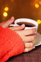 Hands holding mug of hot drink, close-up, on bright background