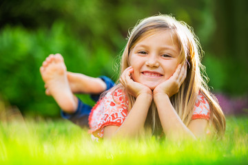 Portrait of a smiling little girl lying on green grass