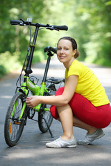Fototapeta na wymiar Young woman in sport clothes sits near bike and smiles in park