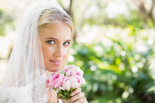 Smiling bride wearing veil holding bouquet looking at camera