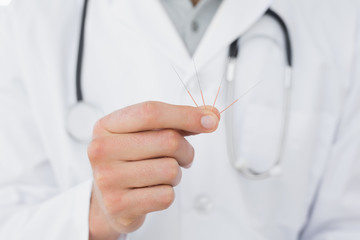Mid section of a male doctor holding acupuncture needles - obrazy, fototapety, plakaty