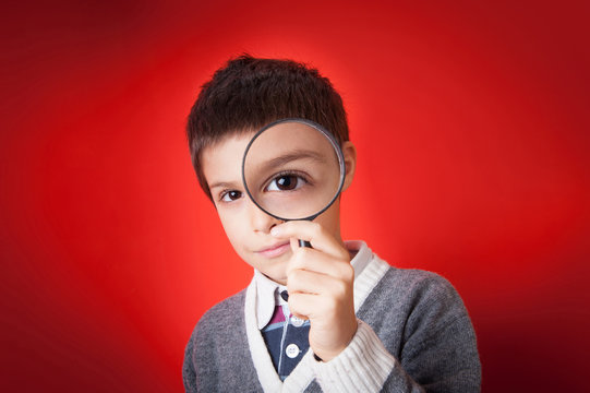 Child looking through a magnifying glass against red background.