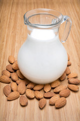 Glass jug with almond milk on a brown wooden table
