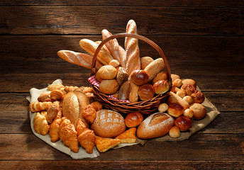 Variety of bread in wicker basket on old wooden background.