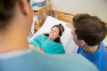 Pregnant Woman Looking At Nurse By Husband In Hospital