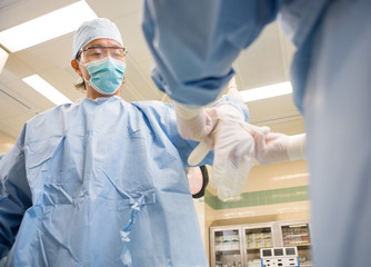 Nurse Assisting Doctor In Wearing Surgical Glove