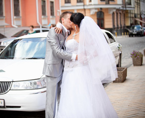 portrait of bride and groom kissing in front of white limousine