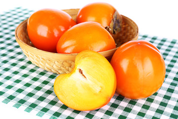 Ripe persimmons in wicker basket on table on white background