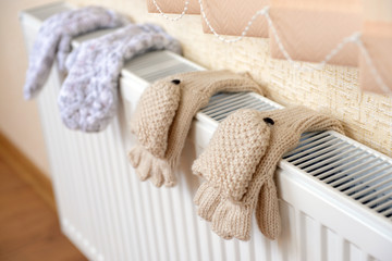 Knitted gloves drying on heating radiator - obrazy, fototapety, plakaty