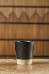 Black ceramic cup on wooden table in bamboo screen (Still life)