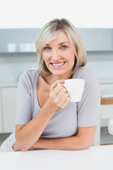 Smiling casual young woman with coffee cup in kitchen