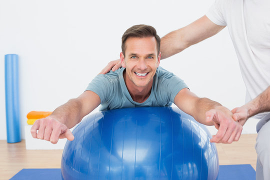 Physical Therapist Assisting Young Man With Yoga Ball