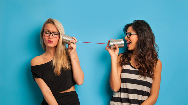 Blonde and brunette women talking with tin can telephone against