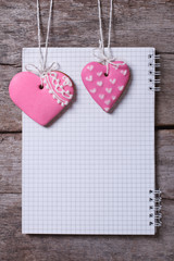 Two pink heart cookies and a note on a wooden board. vertical