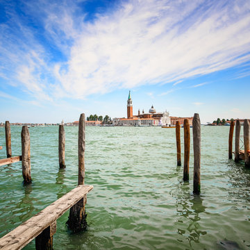 Venice lagoon, wooden poles and church on background. Italy