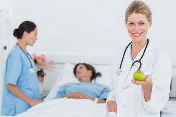 Smiling doctor holding apple with patient in hospital