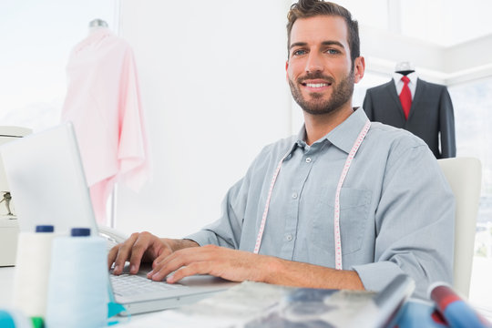 Smiling male fashion designer using laptop in studio