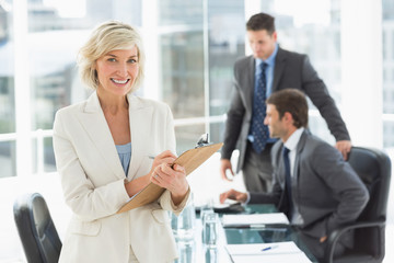 Fototapeta premium Businesswoman writing on clipboard with colleagues in background