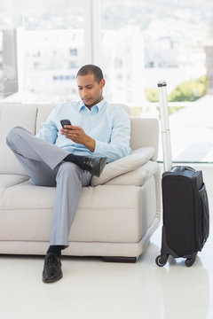Businessman sending a text sitting on sofa waiting to depart on