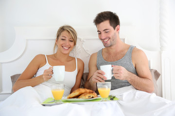 Obraz na płótnie Canvas Cheerful young couple having breakfast in bed