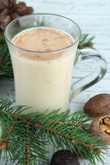 Cup of eggnog with fir branches on wooden background