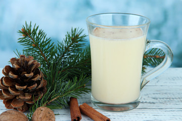 Cup of eggnog with fir branches on table on bright background
