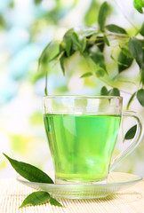 Transparent cup of green tea on bamboo mat, on nature