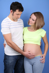 Young pregnant woman with her husband on blue background