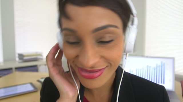 Happy African American business woman listening to music at work