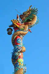 Golden dragon statue on red pillar against blue sky